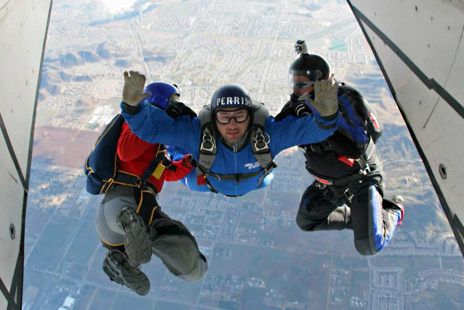 A skydiver jumps from a plane with two guides.