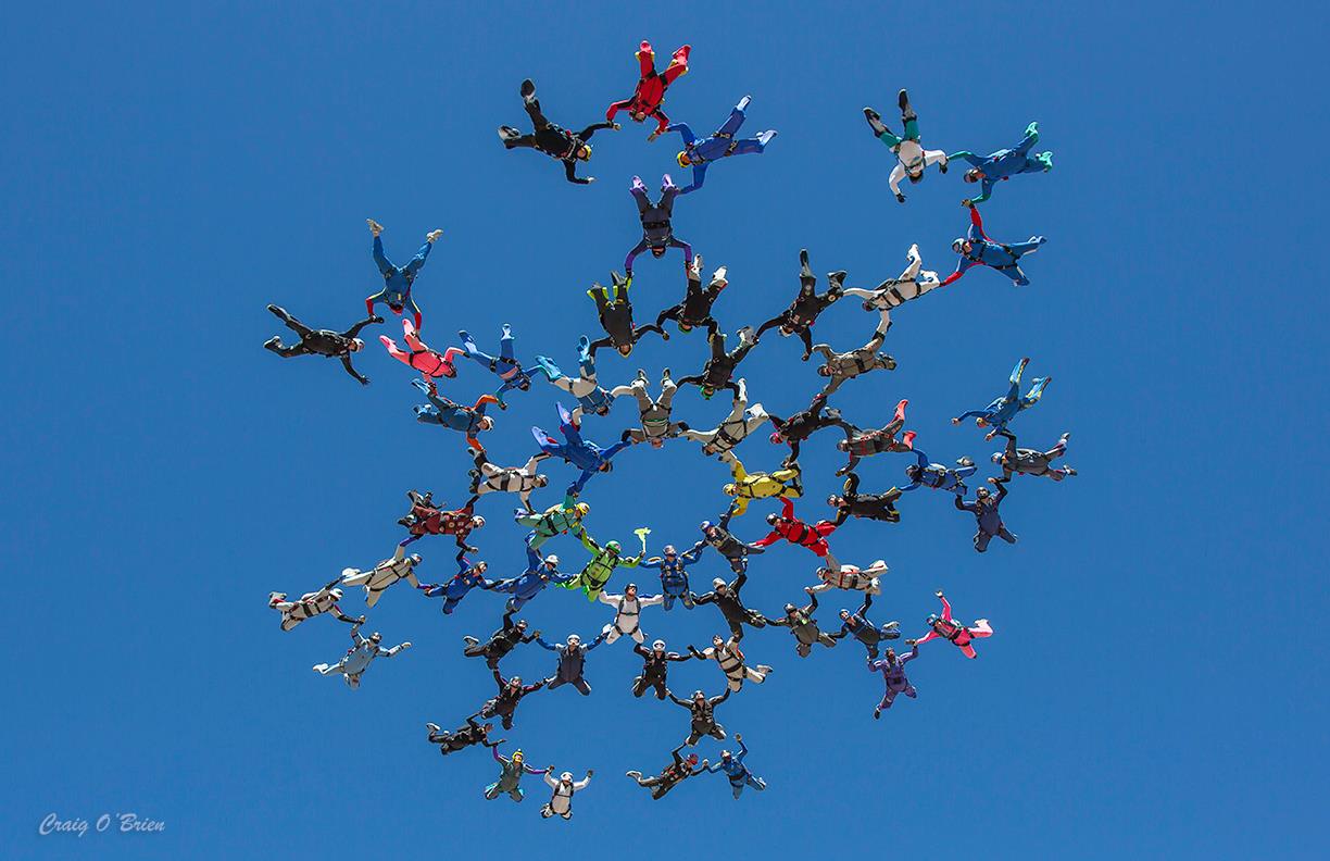 More than a dozen skydivers fly in formation.