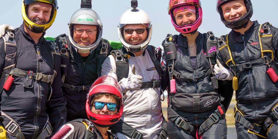 A group of six jumpers smile together before boarding a jump airplane.