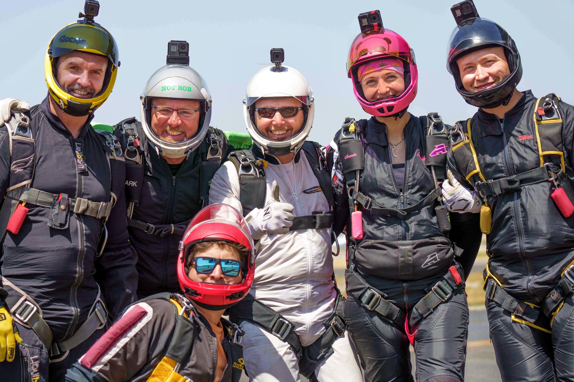 A group of six jumpers smile together before boarding a jump airplane. 